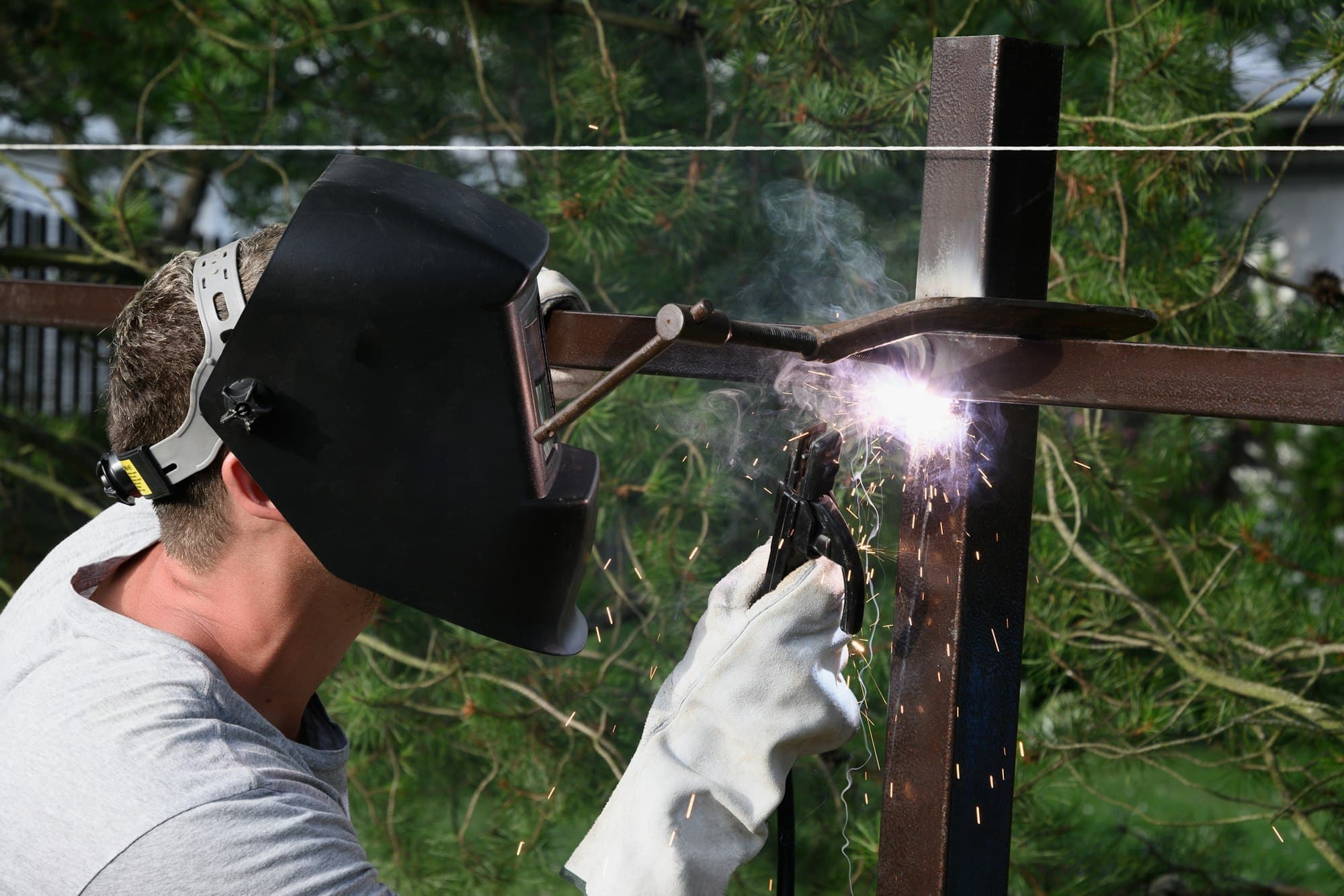 A man in a protective mask and special gloves is construction a metal fence welding.