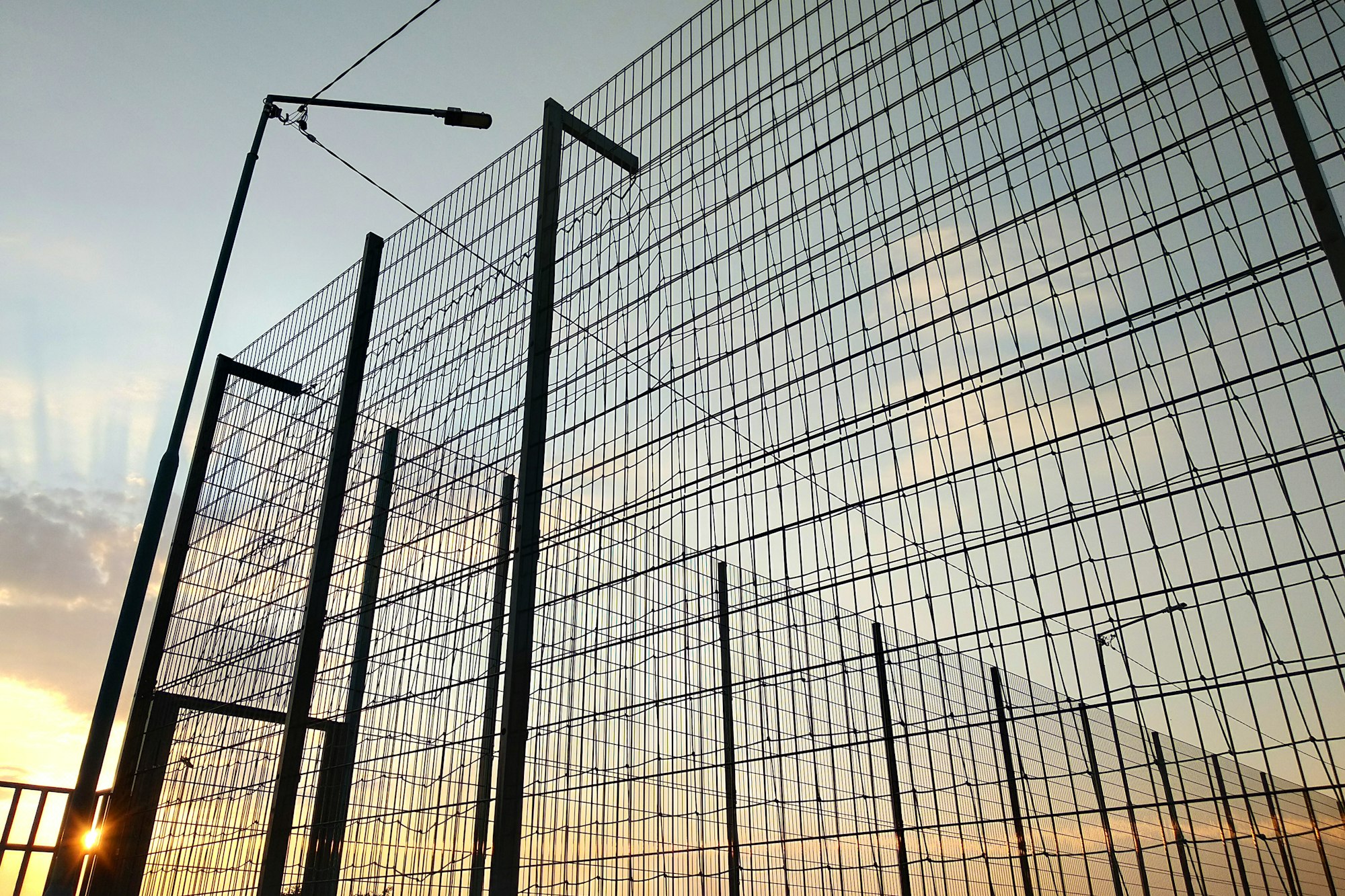 青い空を背景に制限区域の高いワイヤー メッシュ フェンス。