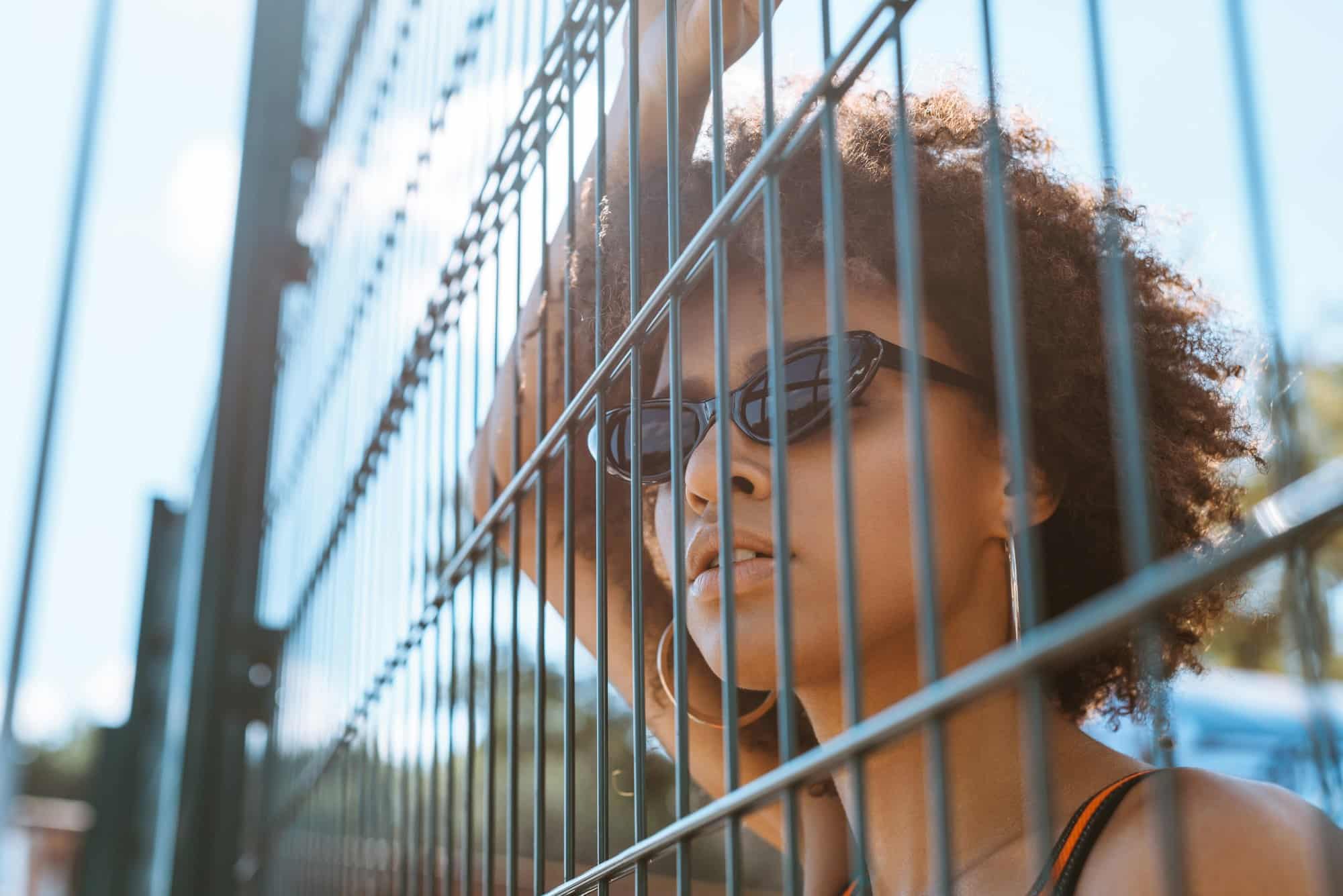 Junge afroamerikanische Frau mit Sonnenbrille posiert hinter einem Drahtzaun