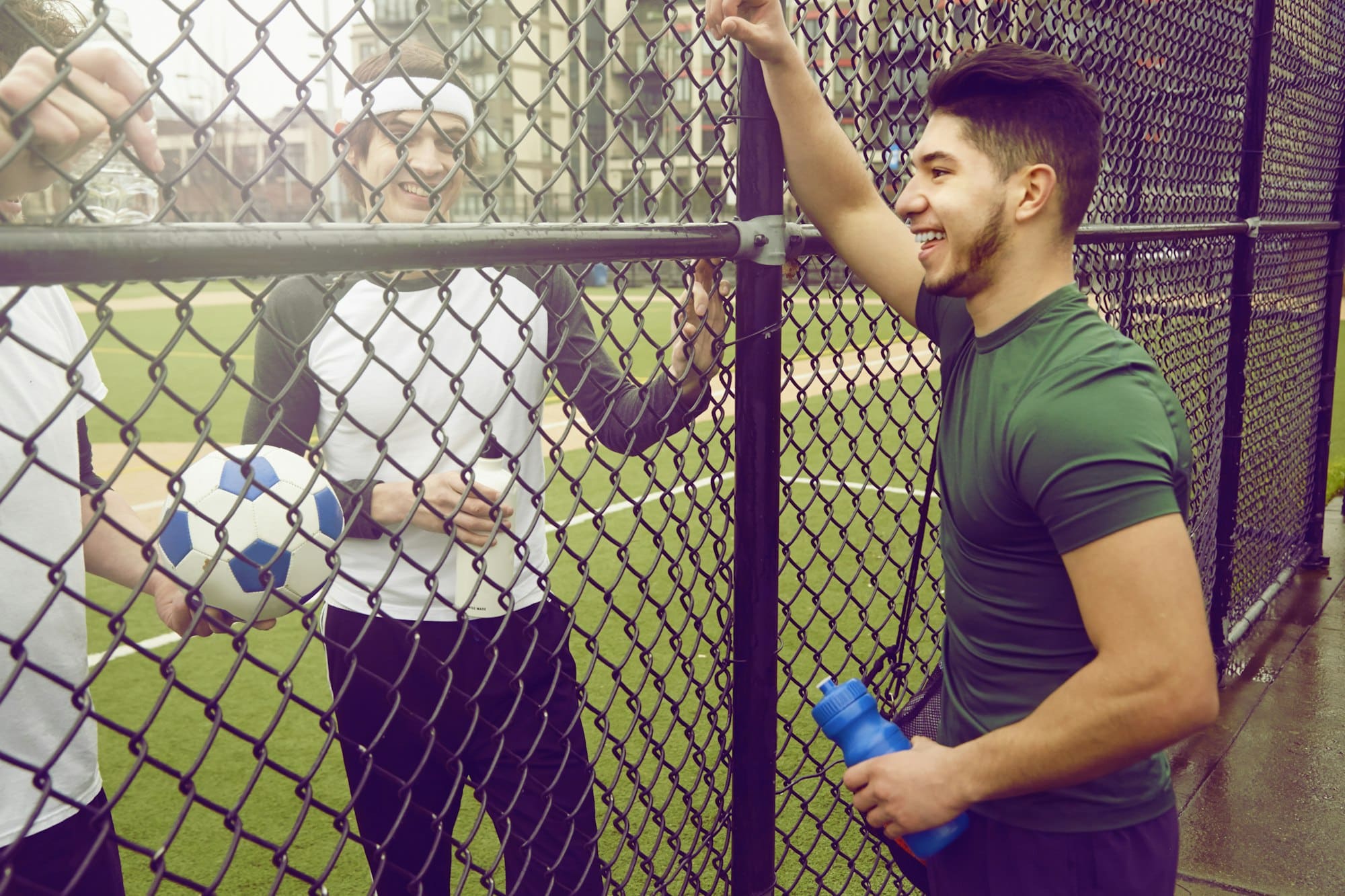 Three male soccer players chatting through wire fence