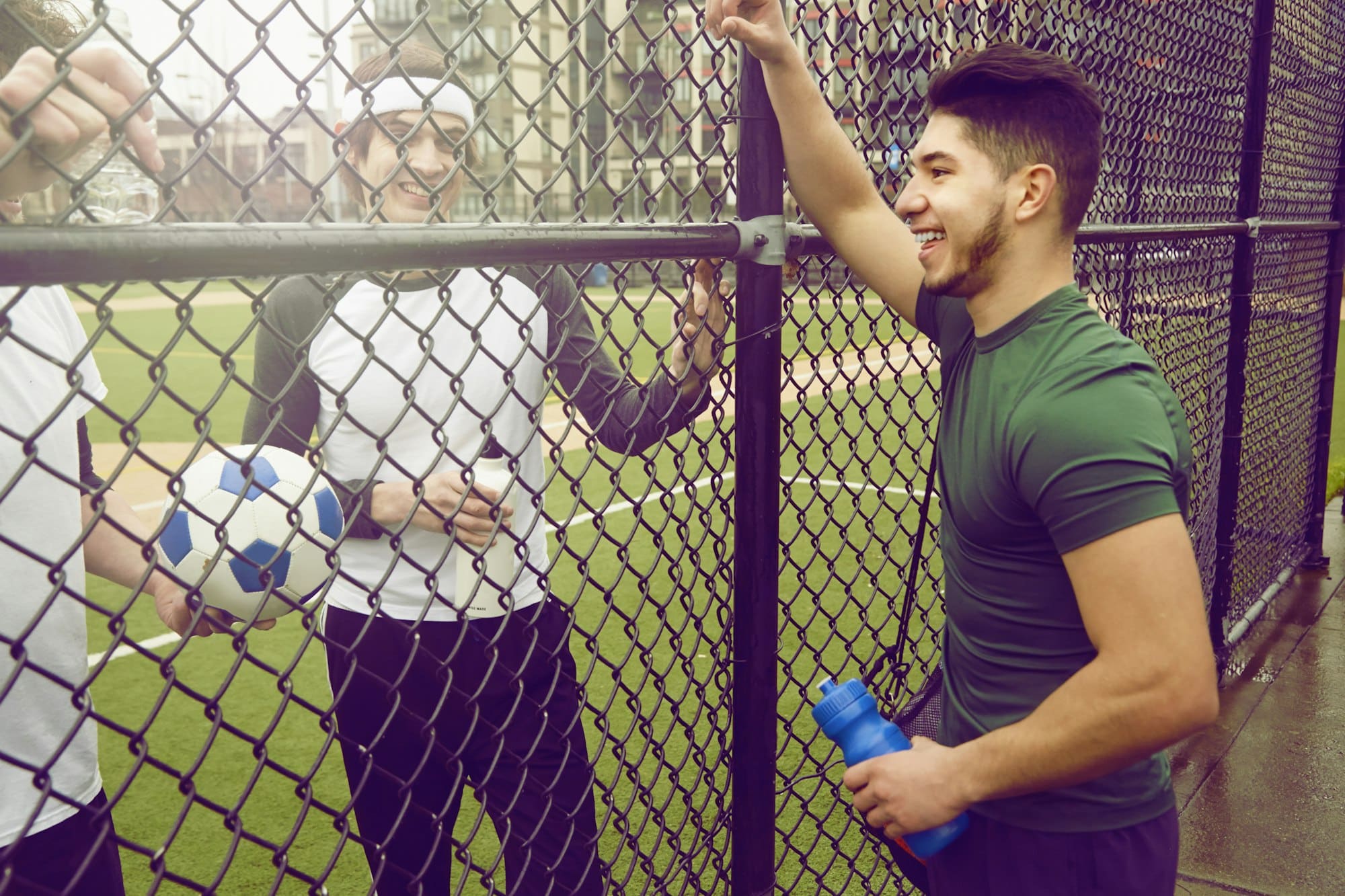 Três jogadores de futebol masculinos conversando através de cerca de arame